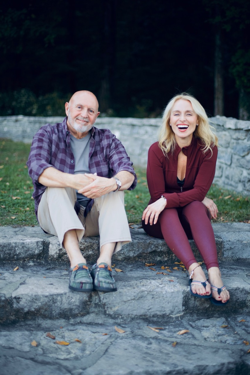 A man and woman sitting on stone steps near grass smiling and looking at camera